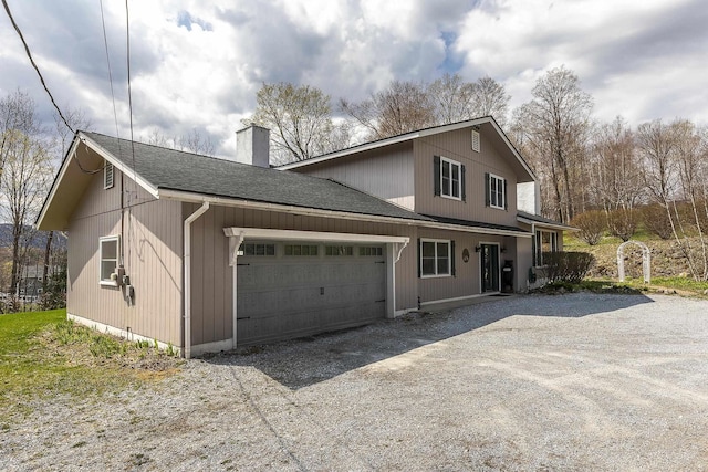 exterior space featuring roof with shingles, dirt driveway, an attached garage, and a chimney