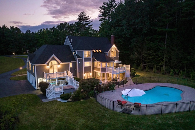 back of house at dusk with a yard, stairway, fence, a fenced in pool, and a balcony