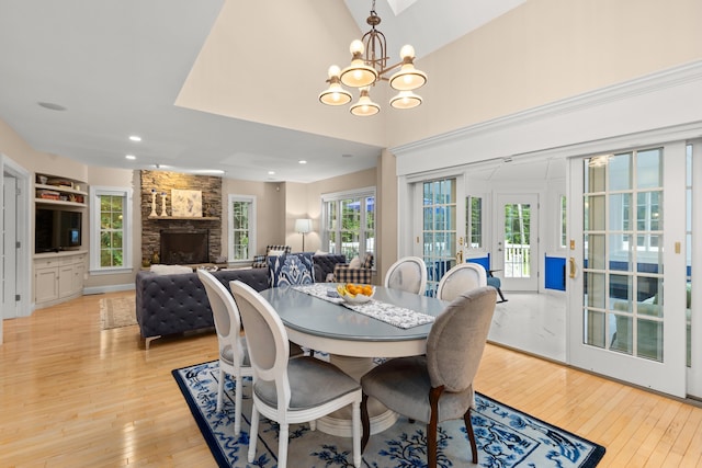 dining space with recessed lighting, light wood-style floors, a notable chandelier, a stone fireplace, and french doors