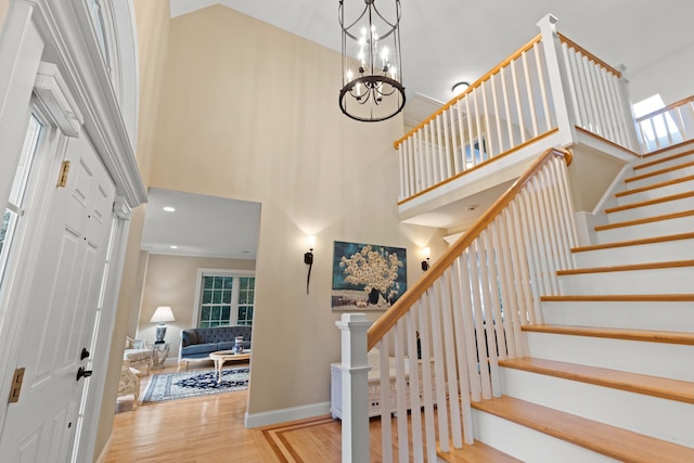 stairway with a towering ceiling, wood finished floors, a chandelier, and baseboards