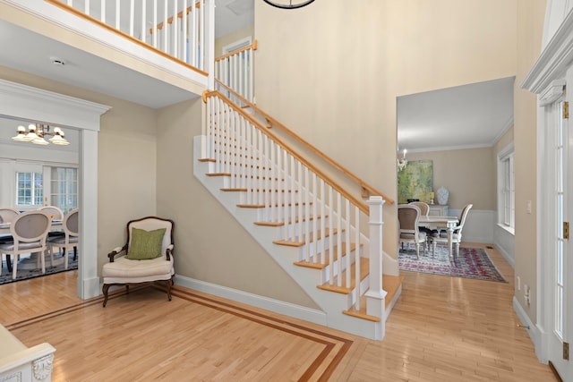 stairway featuring crown molding, a chandelier, baseboards, wood finished floors, and a high ceiling