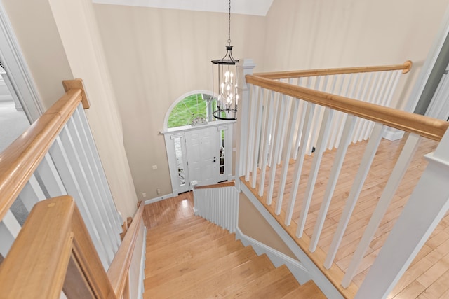 staircase featuring baseboards, wood finished floors, an inviting chandelier, and a high ceiling