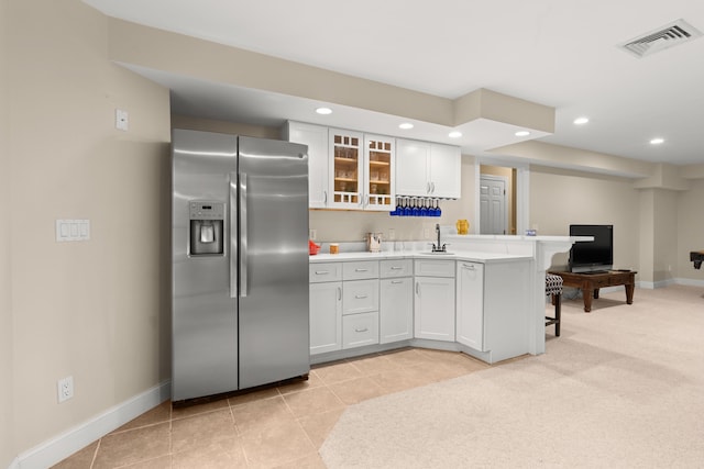 kitchen with a sink, stainless steel fridge, a kitchen bar, visible vents, and baseboards