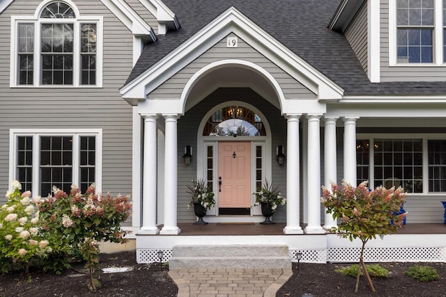 view of exterior entry featuring a porch and a shingled roof