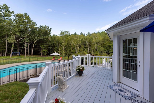 wooden deck with a fenced in pool, a forest view, and fence