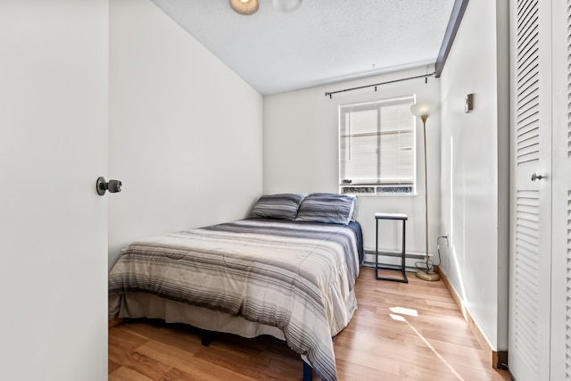 bedroom featuring lofted ceiling, light wood finished floors, a baseboard heating unit, and baseboards