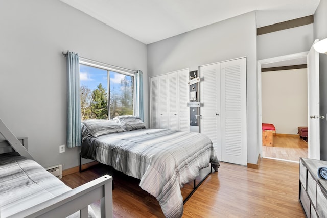 bedroom featuring two closets, light wood-type flooring, a baseboard heating unit, and baseboards