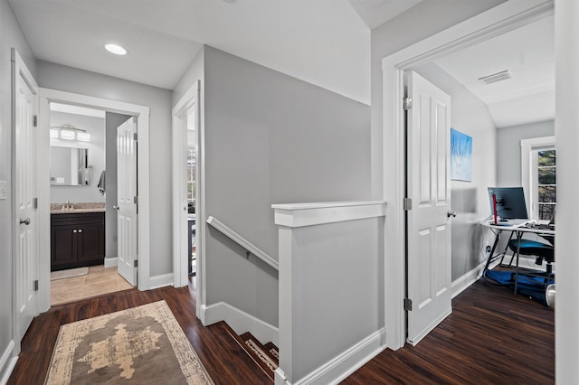 hall featuring a sink, an upstairs landing, visible vents, and wood finished floors