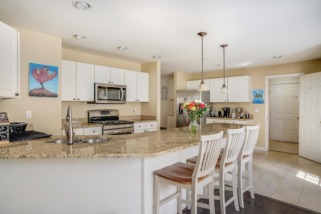 kitchen with white cabinetry, a sink, stainless steel appliances, light stone countertops, and a peninsula