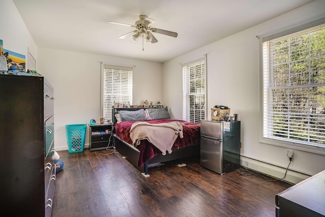 bedroom featuring multiple windows, baseboard heating, freestanding refrigerator, and wood finished floors