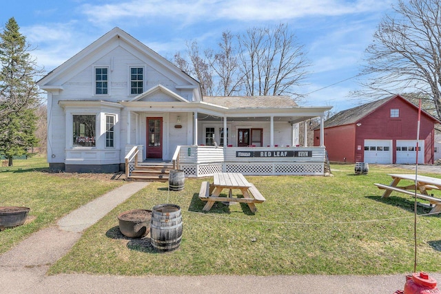 view of front of house featuring covered porch, a front yard, an outbuilding, and a garage