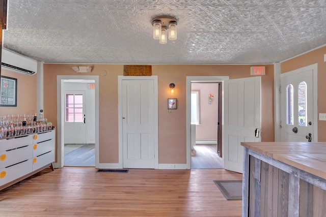 interior space with a baseboard heating unit, light wood finished floors, wood counters, a wall mounted AC, and an ornate ceiling