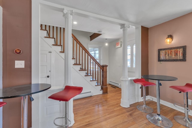 interior space with light wood-style flooring, stairs, baseboard heating, and decorative columns