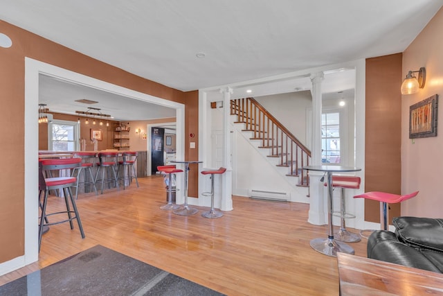 interior space featuring bar, a baseboard radiator, baseboards, ornate columns, and wood finished floors