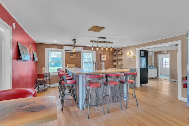 kitchen featuring a breakfast bar area, plenty of natural light, a wall mounted air conditioner, and light wood-style flooring