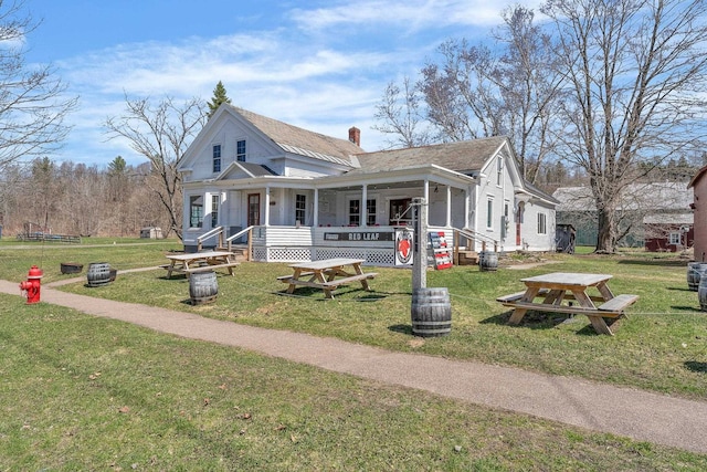 view of front of house featuring covered porch, a chimney, and a front lawn