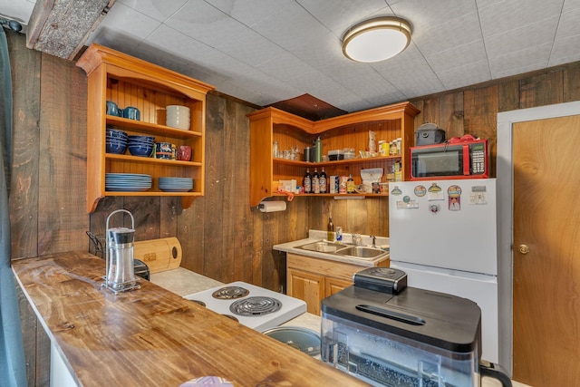 kitchen with wood walls, open shelves, freestanding refrigerator, and a sink