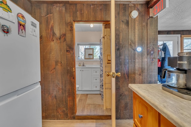 interior space with a sink, light countertops, freestanding refrigerator, wooden walls, and light wood-type flooring