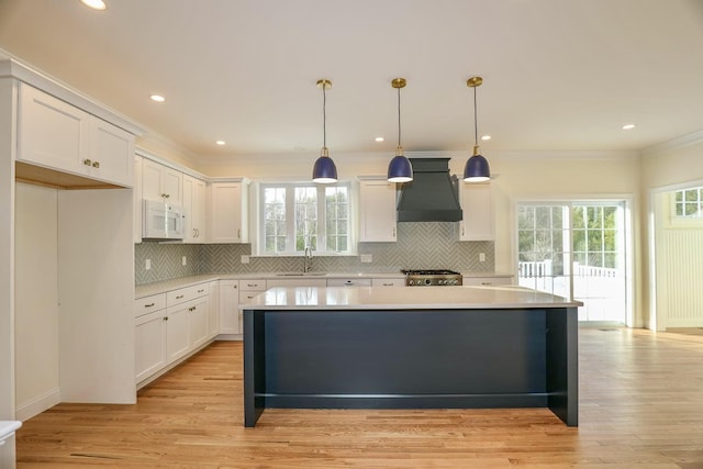 kitchen with custom exhaust hood, range, white microwave, light countertops, and ornamental molding