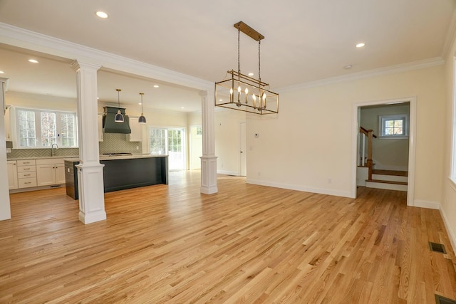 unfurnished dining area with light wood-style flooring, a sink, decorative columns, and visible vents