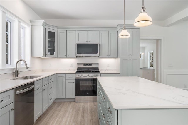 kitchen featuring a sink, light wood-type flooring, light stone counters, a kitchen island, and appliances with stainless steel finishes