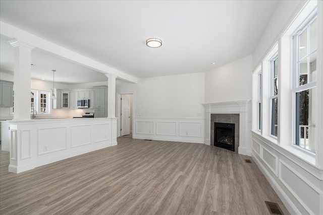 unfurnished living room featuring a tile fireplace, visible vents, plenty of natural light, and light wood finished floors