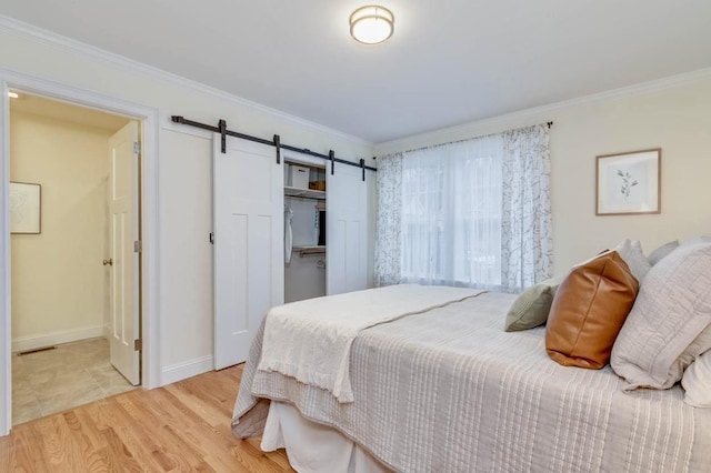 bedroom with wood finished floors, a barn door, ornamental molding, and a closet
