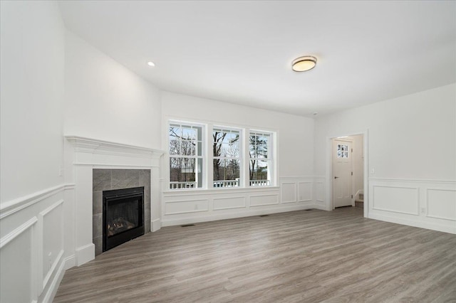 unfurnished living room with a tiled fireplace, wood finished floors, a wainscoted wall, and a decorative wall