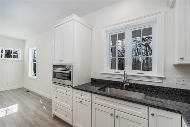 kitchen featuring a sink, light wood-style floors, dark stone countertops, white cabinets, and stainless steel oven