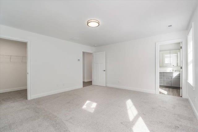 unfurnished bedroom with a spacious closet, ensuite bathroom, carpet flooring, baseboards, and visible vents