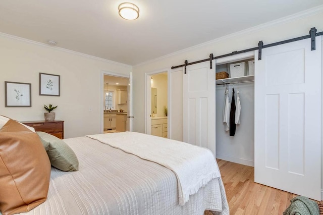 bedroom featuring connected bathroom, a barn door, light wood-style floors, a closet, and ornamental molding