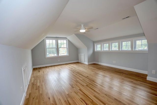 additional living space with light wood-type flooring, a ceiling fan, visible vents, baseboards, and lofted ceiling