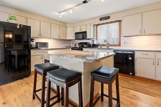 kitchen with a sink, tasteful backsplash, black appliances, a breakfast bar area, and light wood-style flooring