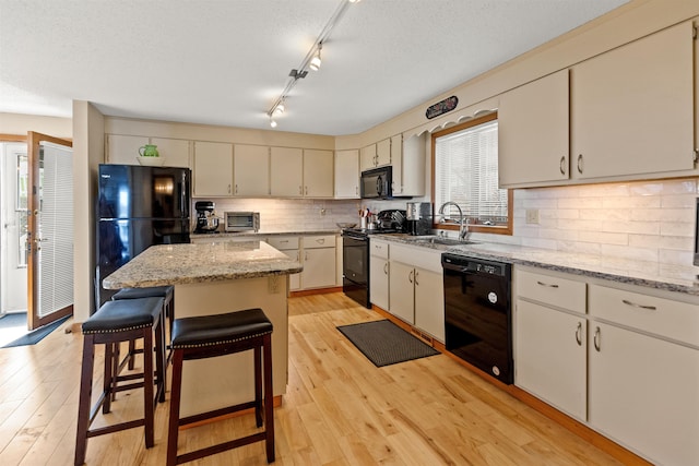 kitchen with light wood-type flooring, black appliances, a kitchen island, and a sink