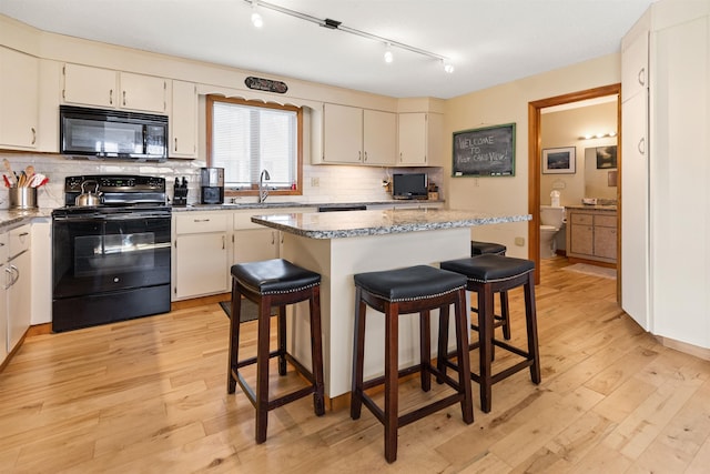 kitchen with a breakfast bar, light wood-type flooring, black appliances, and tasteful backsplash