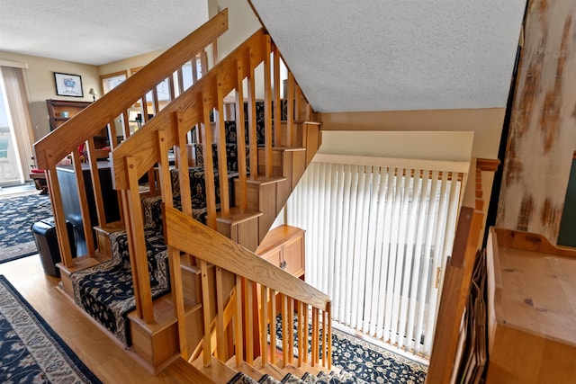 stairway featuring a textured ceiling, a wealth of natural light, and wood finished floors