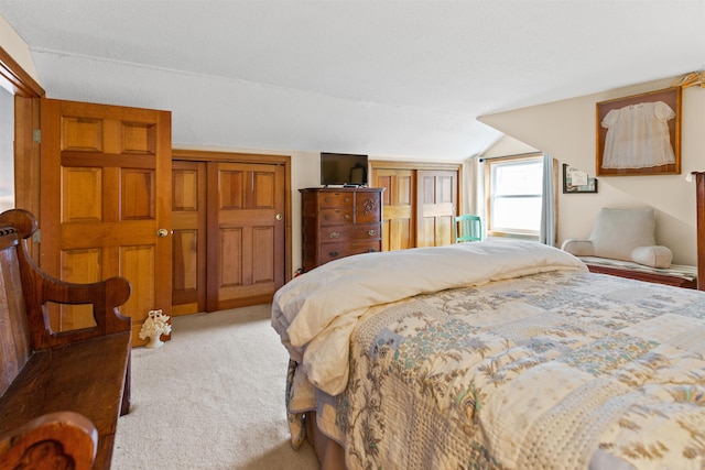 carpeted bedroom featuring multiple closets and vaulted ceiling