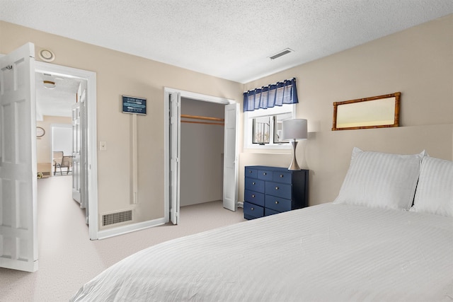bedroom with a textured ceiling, visible vents, light colored carpet, and a closet