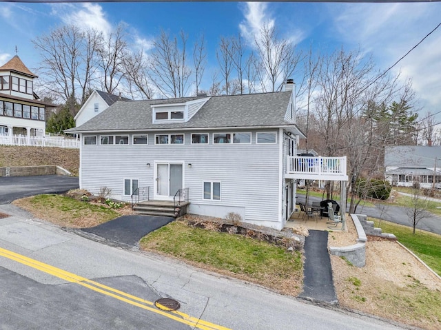 view of front of house with a chimney, a wooden deck, a shingled roof, and a patio area