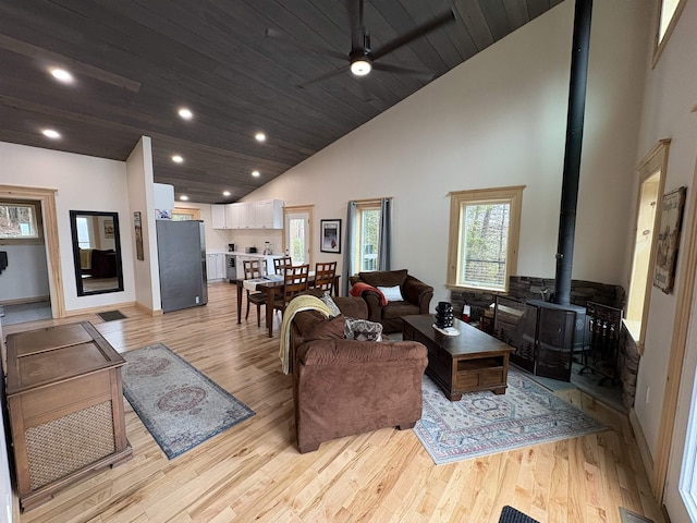 living room featuring a wood stove, a ceiling fan, high vaulted ceiling, and light wood-style floors