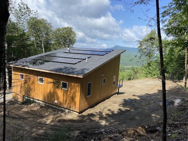 view of side of home featuring solar panels and roof with shingles