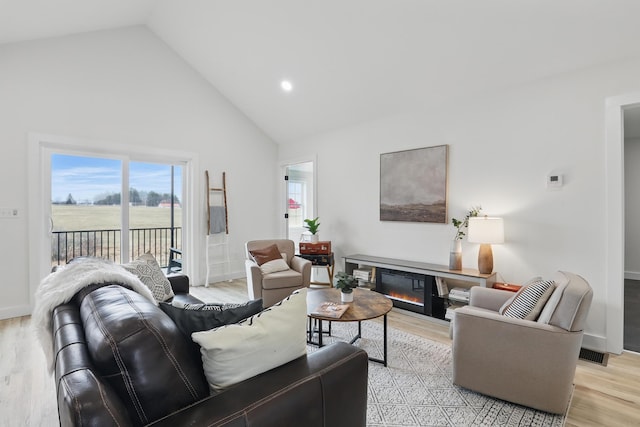 living room with baseboards, high vaulted ceiling, light wood-type flooring, and a glass covered fireplace