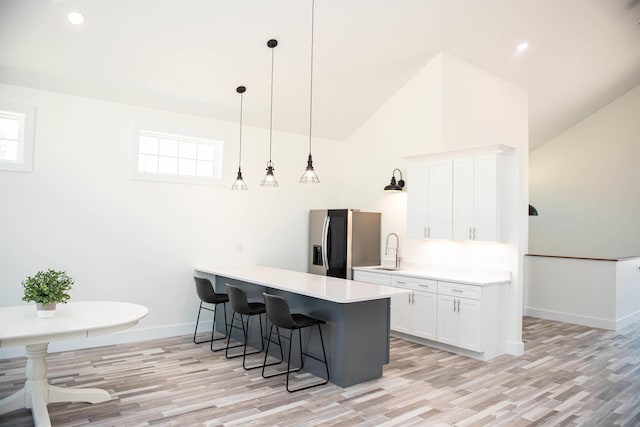 kitchen with a breakfast bar, stainless steel refrigerator with ice dispenser, white cabinetry, a peninsula, and baseboards
