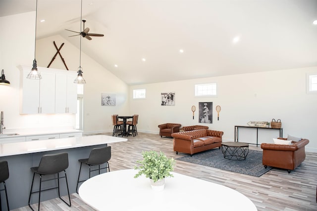 living room featuring light wood finished floors, high vaulted ceiling, and baseboards