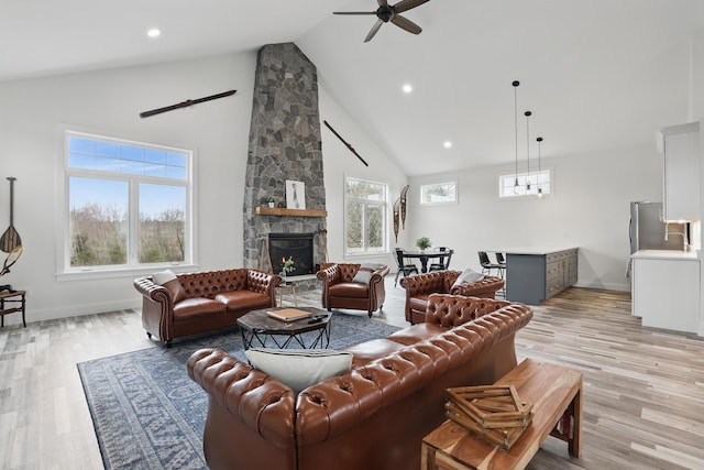 living area with light wood-style flooring, a stone fireplace, baseboards, high vaulted ceiling, and a ceiling fan