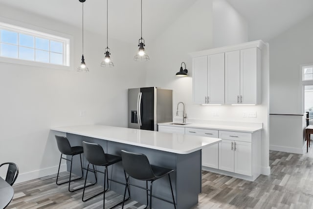 kitchen with a breakfast bar area, light wood-style flooring, a sink, stainless steel refrigerator with ice dispenser, and high vaulted ceiling