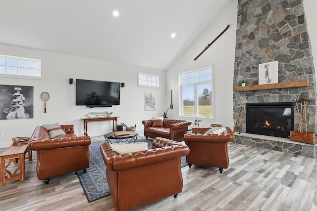 living room with light wood-style floors, recessed lighting, high vaulted ceiling, and a stone fireplace