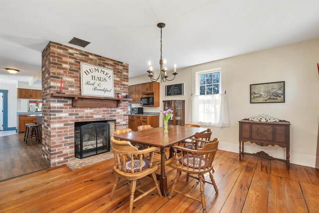 7449 School St, Loudon, NH 03307 - dining area with visible vents, baseboards, an inviting chandelier, light wood finished floors, and a brick fireplace