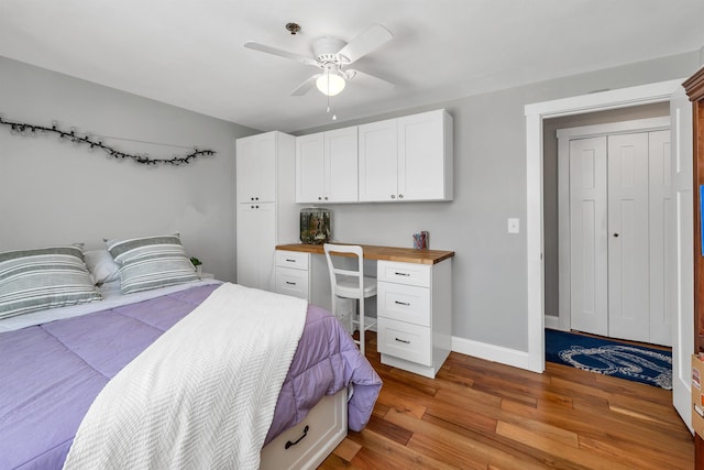 bedroom with a closet, baseboards, built in study area, light wood-type flooring, and a ceiling fan