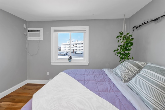 bedroom with wood finished floors, a wall unit AC, and baseboards